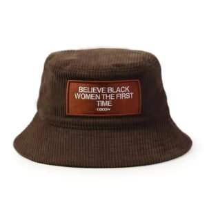 Brown corduroy bucket hat with front embroidered patch reading “Believe Black Women The First Time.”